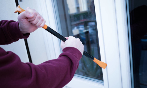 Hooded burglar forcing window lock to make a theft in a house